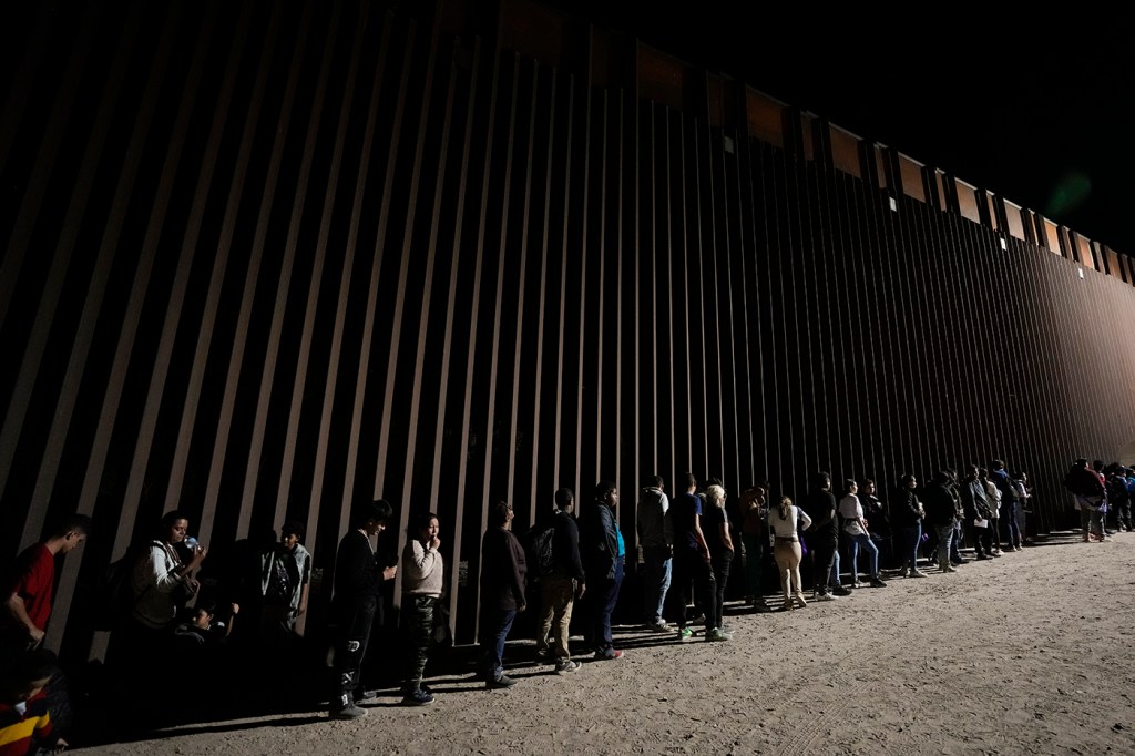 A line of immigrants at the border wall.