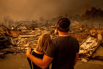 Two people standing, one with their arm around the other, looking at the damage the fires caused.