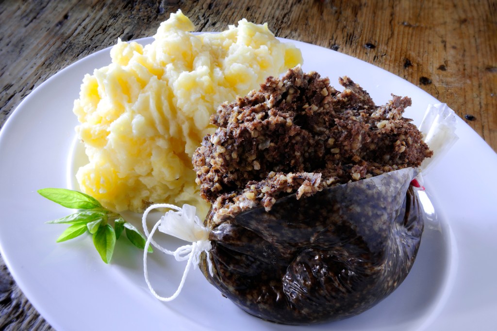 A plate of Haggis next to mashed potatoes.