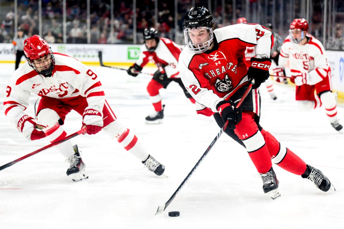 A Northeastern hockey player skating on the ice with the puck.