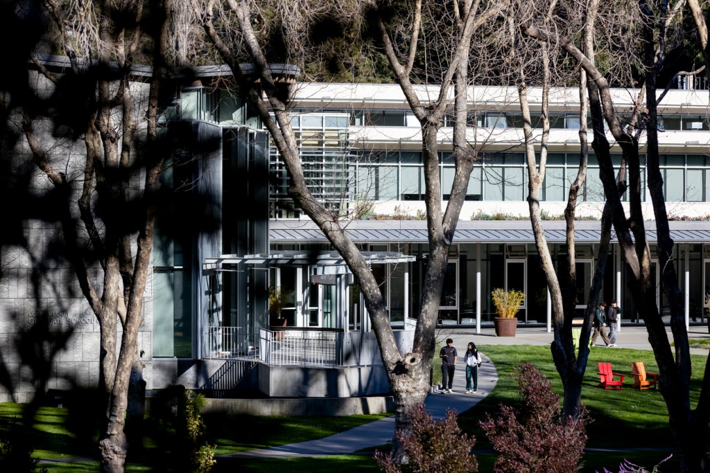 People walk through a serene campus scene with trees and a modern building.