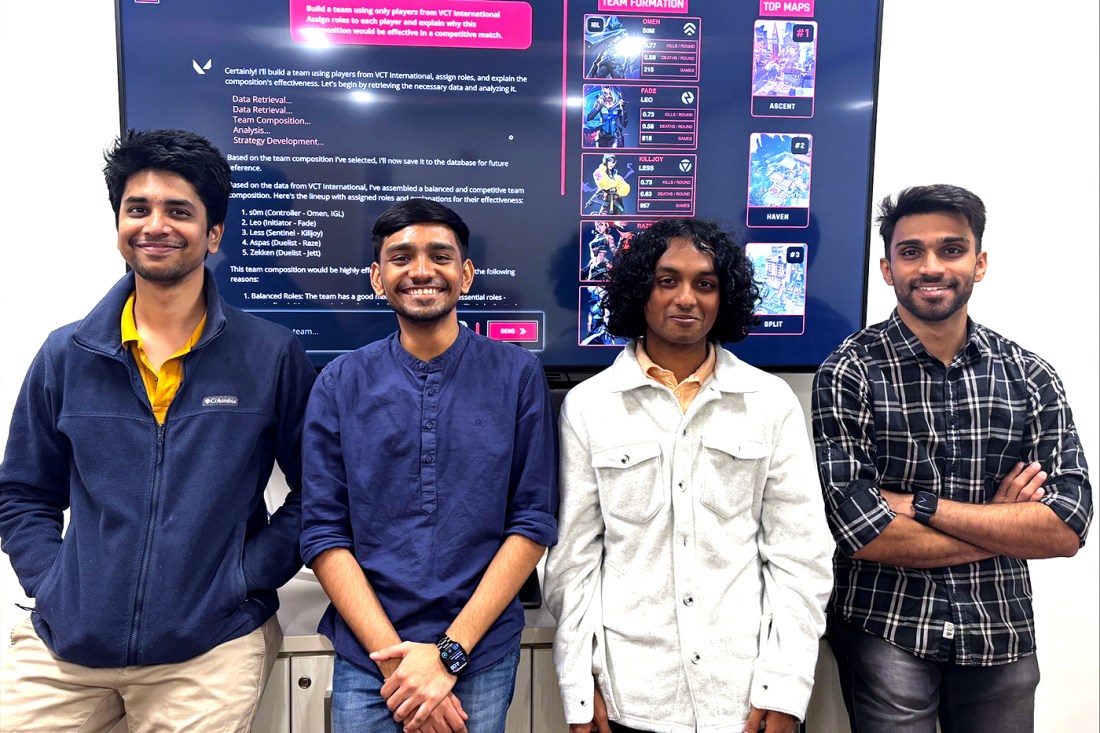 Four students posing together in front of a large screen displaying their project.