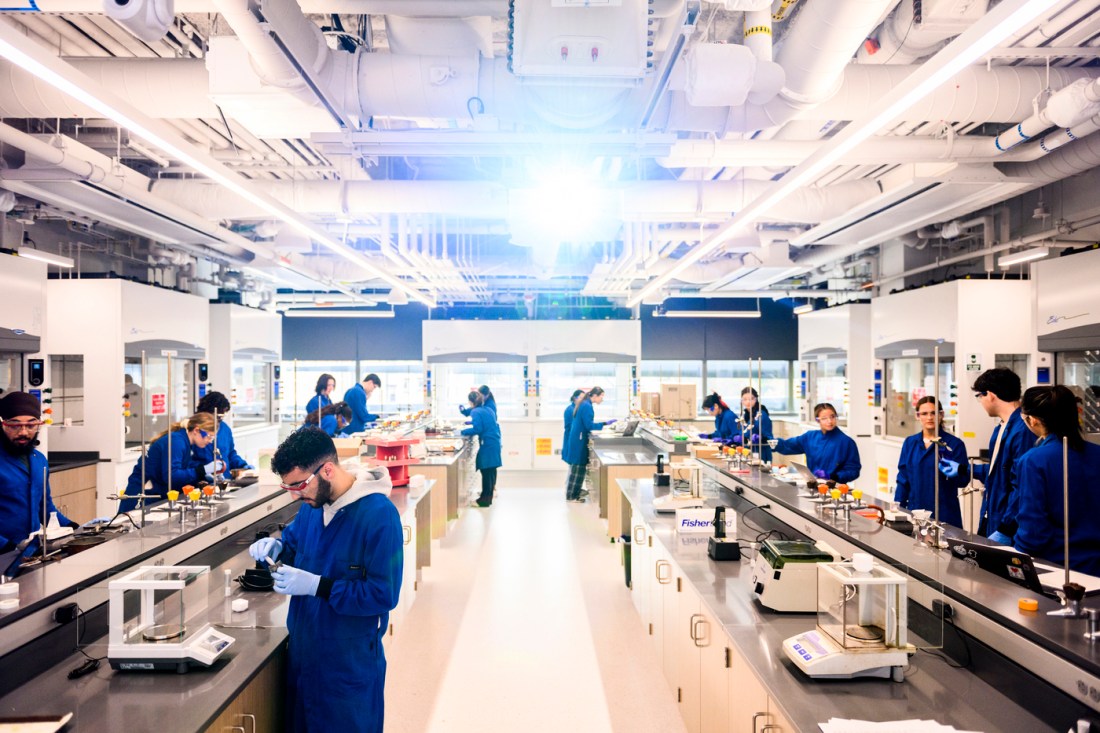 A busy laboratory setting with people in blue lab coats conducting experiments and working at lab stations.