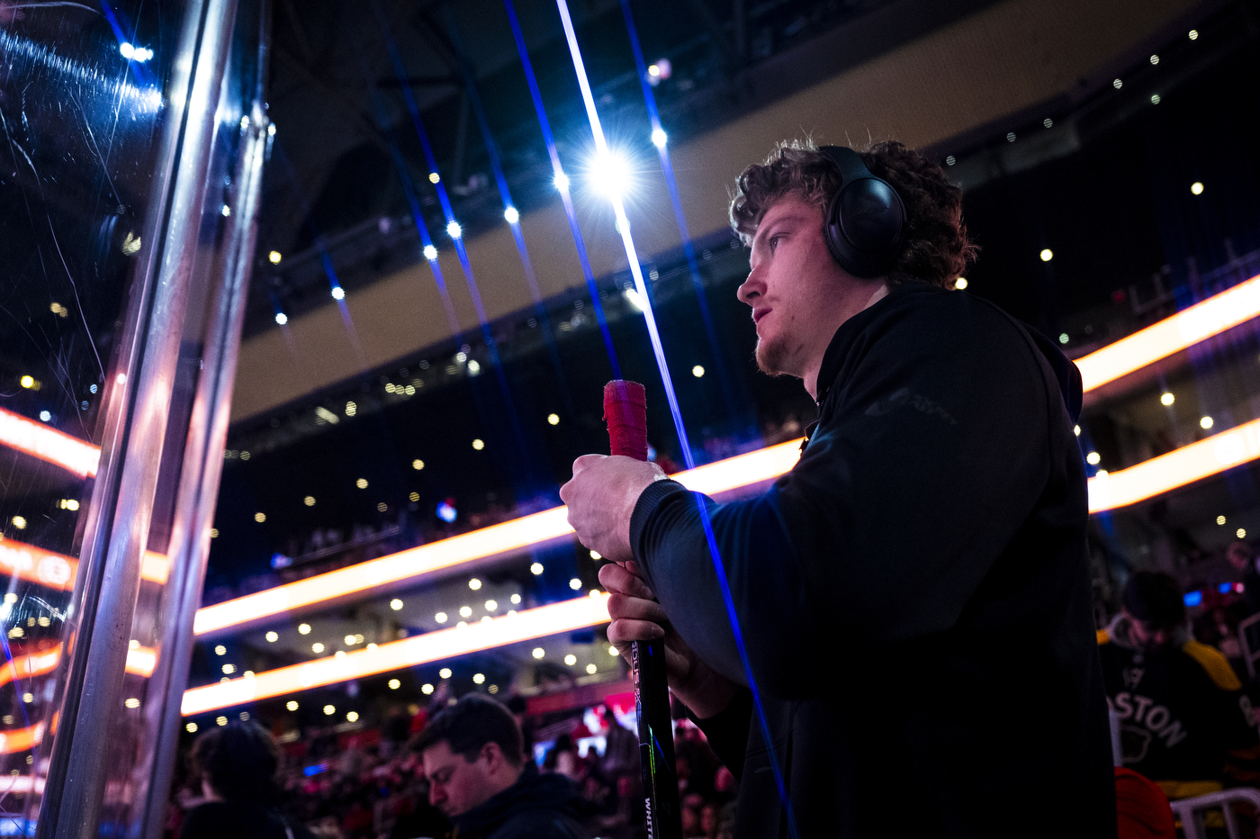 A Northeastern mens hockey player wearing over the ear headphones holding his hockey stick before the game.