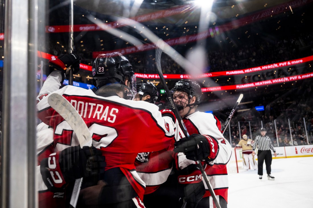 A group of hockey players celebrating on the ice near the glass, wearing red and black jerseys.