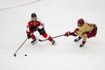 A Northeastern hockey player skates on the ice with the puck while a BC hockey player sticks his hockey stick in the players path.