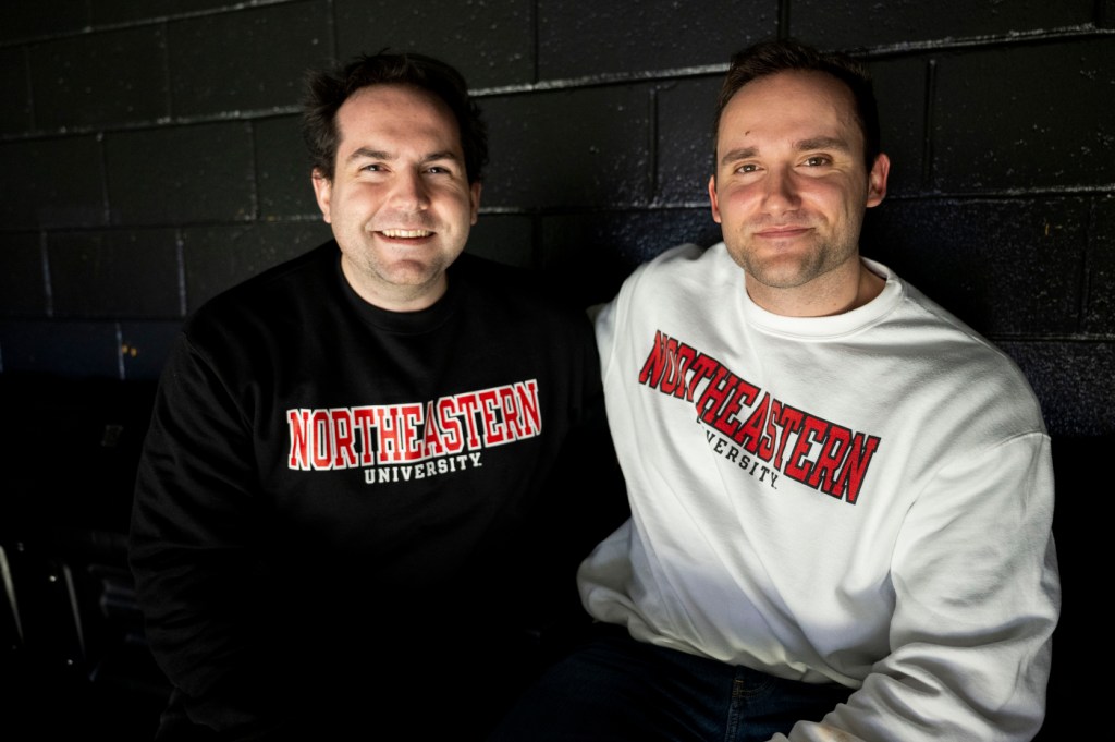 Two people sitting together and smiling, wearing Northeastern sweatshirts.