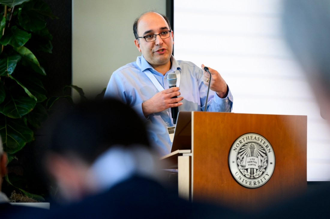 Hessam Mahdavifar wearing a blue button down standing behind a podium speaking into a microphone at a conference.