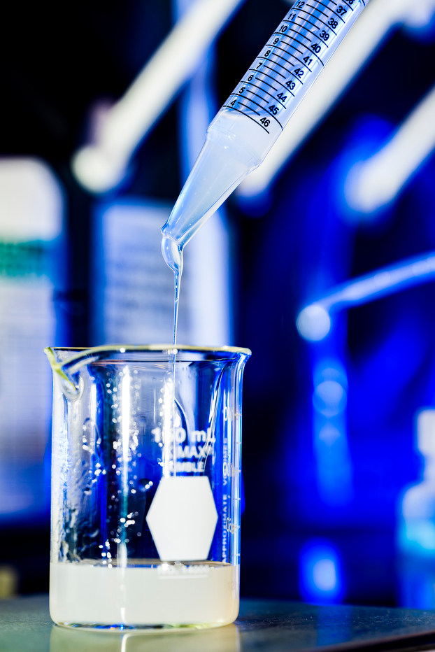 A stream of liquid coming out of a pipette into a beaker in a lab.