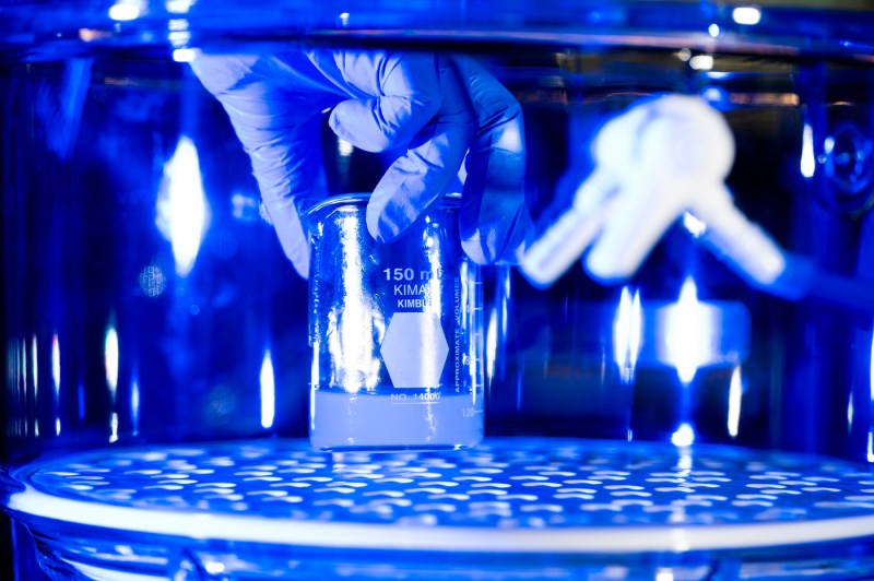 A gloved hand holding a beaker in a blue-lit lab.