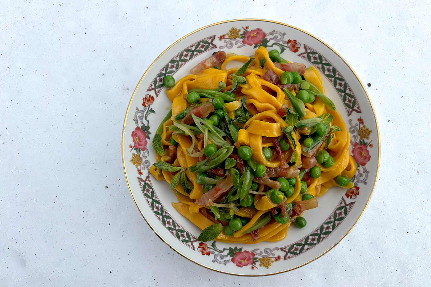 A bowl filled with pasta with peas and pancetta in it and a sprinkle of green leaves. 