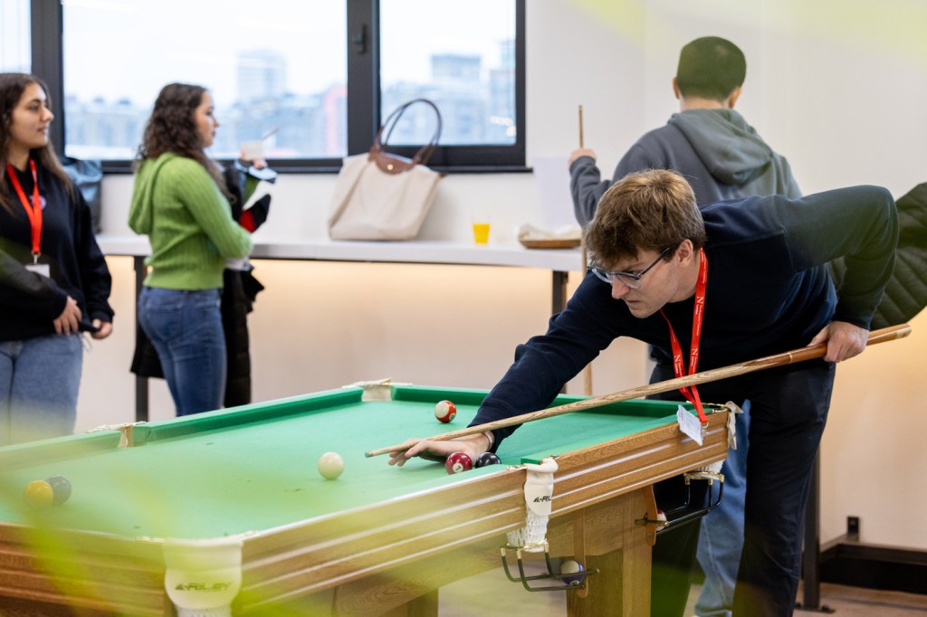 A student holding a cue stick leaning over the billiards table.