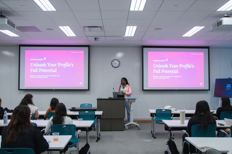 Attendees of the WISE Summit sitting in a room. At the front of a room a person stands at a podium in front of a microphone between two projector screens.