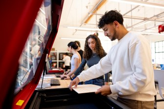 Students work collaboratively in a bright, modern makerspace, using various equipment and tools to complete their projects.