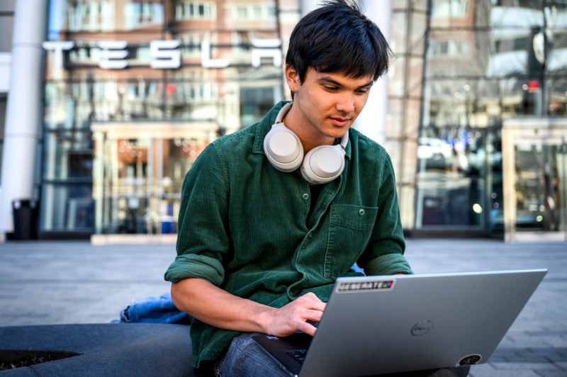 Kaden Du sitting outside in front of a Tesla building working on a laptop.