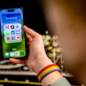 A person holding an iPhone open to a folder of social media apps.