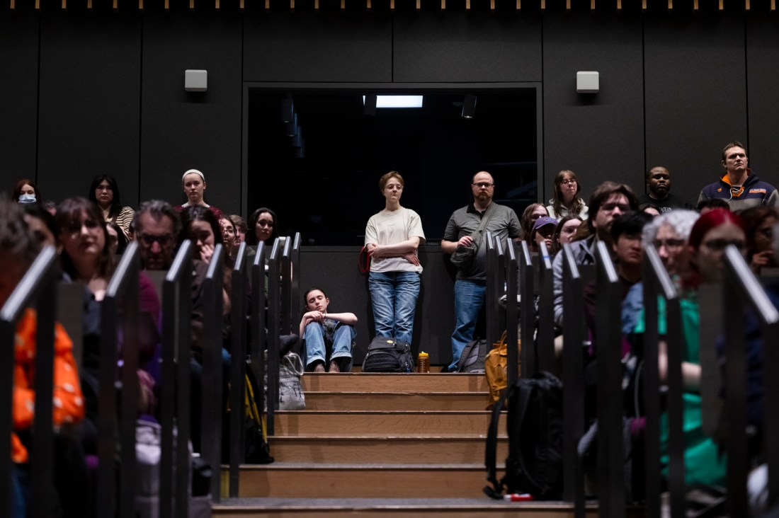 People sitting on the stairs and standing behind the seats of an auditorium.