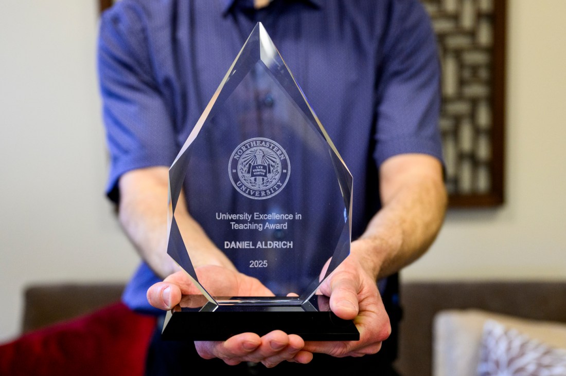 Daniel Aldrich holding a glass award in front of him that says 'University Excellence in Teaching Award DANIEL ALDRICH' on it.