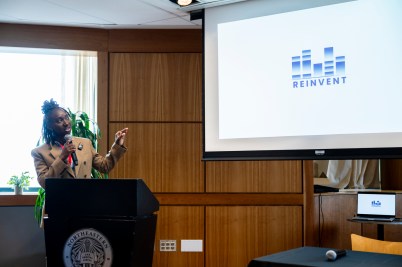 Gabby Aidam speaking in a microphone in front of a slide.