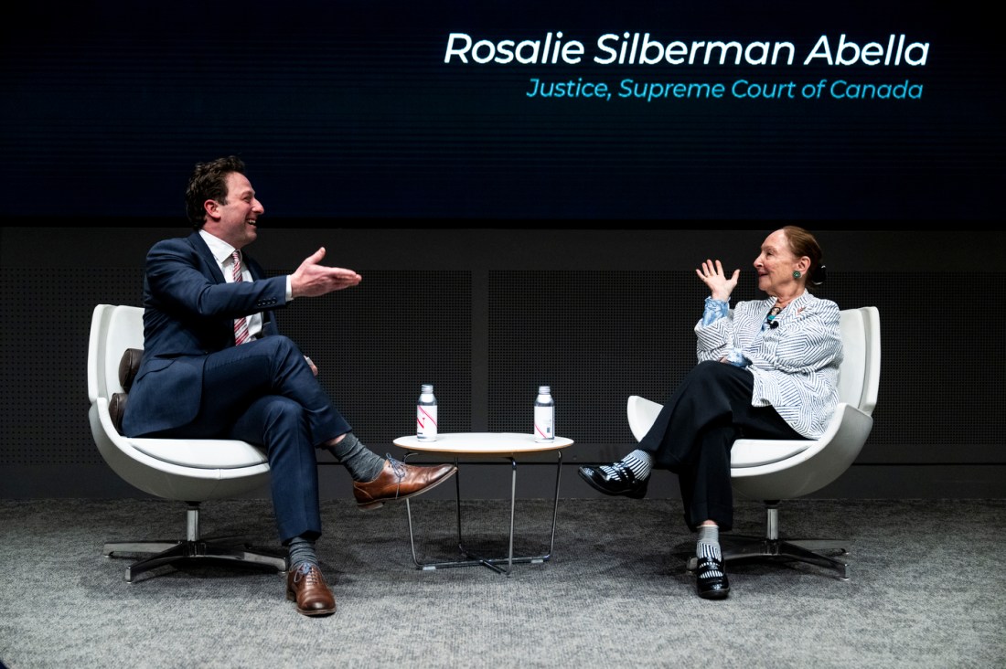 Justice Rosalie Abella speaks with Simon Rabinovitch during the Ruderman Memorial Lecture at Northeastern, with her name and title displayed behind them.
