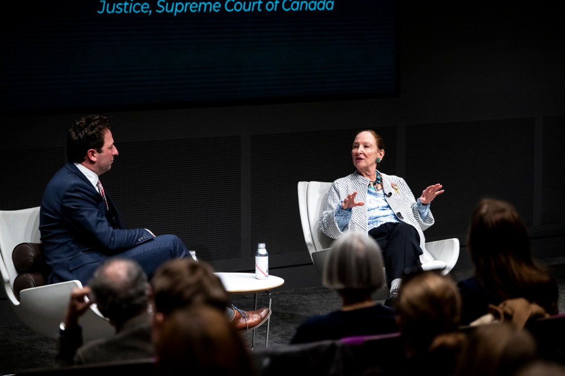 Two people sit on stage in conversation during a public lecture.