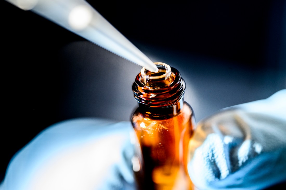 A gloved hand holding a pipette over a test tube.