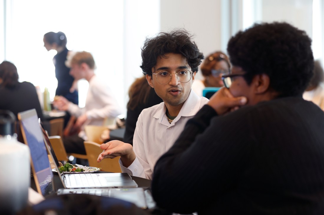 A student speaking with a small business owner while gesturing to a laptop screen.