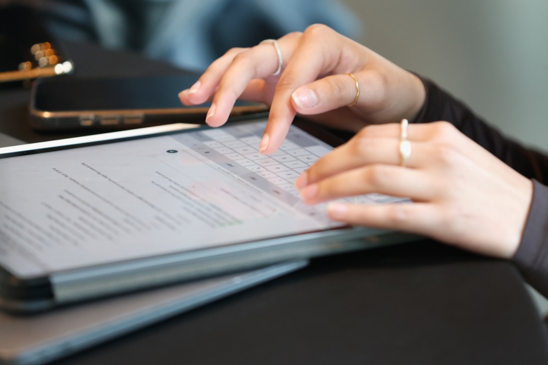 A student's hands typing on an iPad.