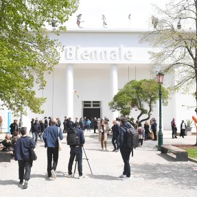Visitors walking in front of a building that says 'Biennale' on it.