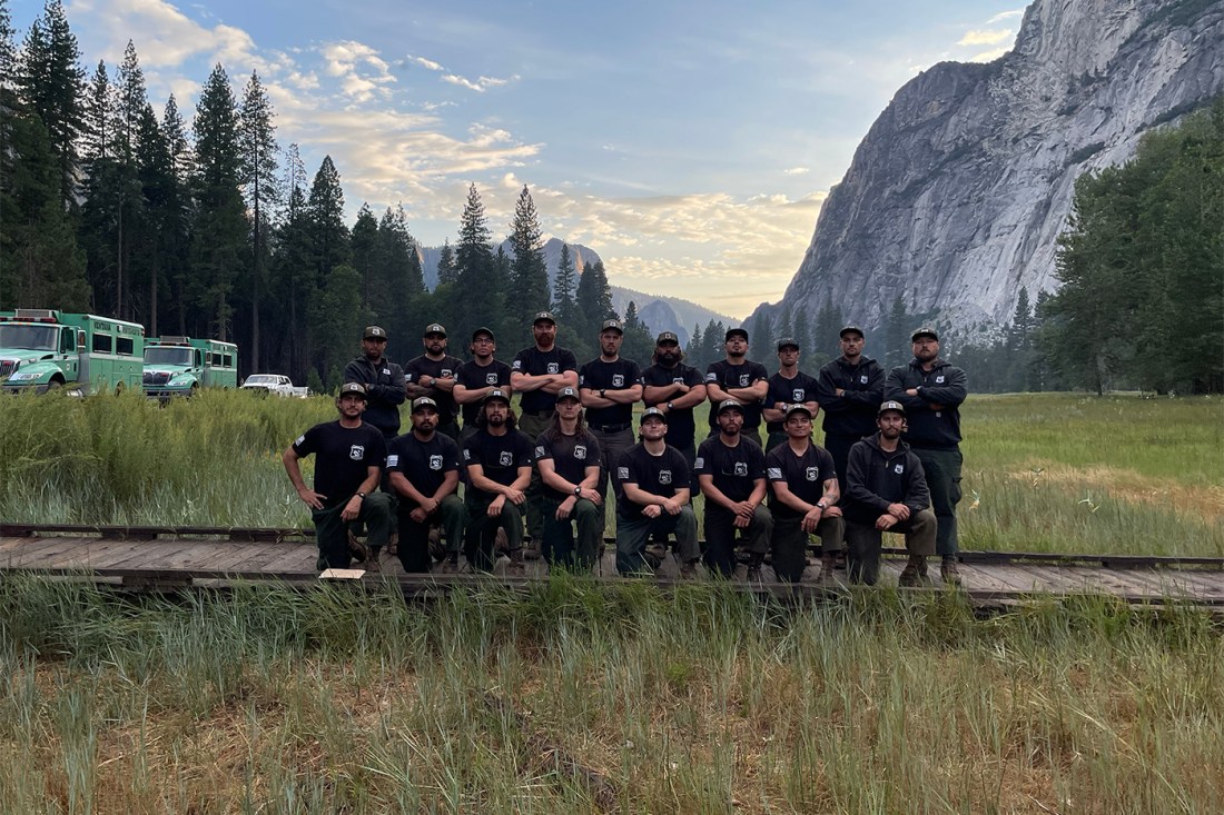 Evan Kenny and a group of other people posing outside in a field of grass in front of a pine forest and a mountain.