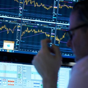 A person working on the floor at the NY Stock Exchange looking at screens displaying graphs.