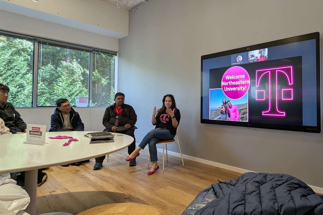 Three people sitting at the front of a room next to a TV screen that has a pink T-mobile logo and the text 'Welcome Northeastern University!'