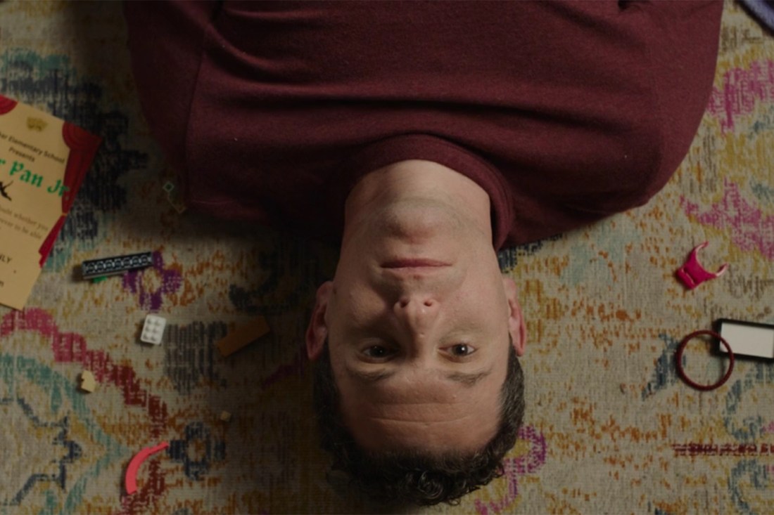 A screen capture from the short film “What It’s Like to Be Okay” that has the camera looking down on a person lying on a carpeted floor with lego pieces surrounding their head.