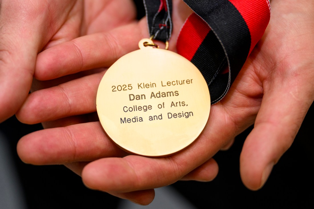 A gold medal engraved to say '2025 Klein Lecturer Dan Adams College of Arts, Media and Design'