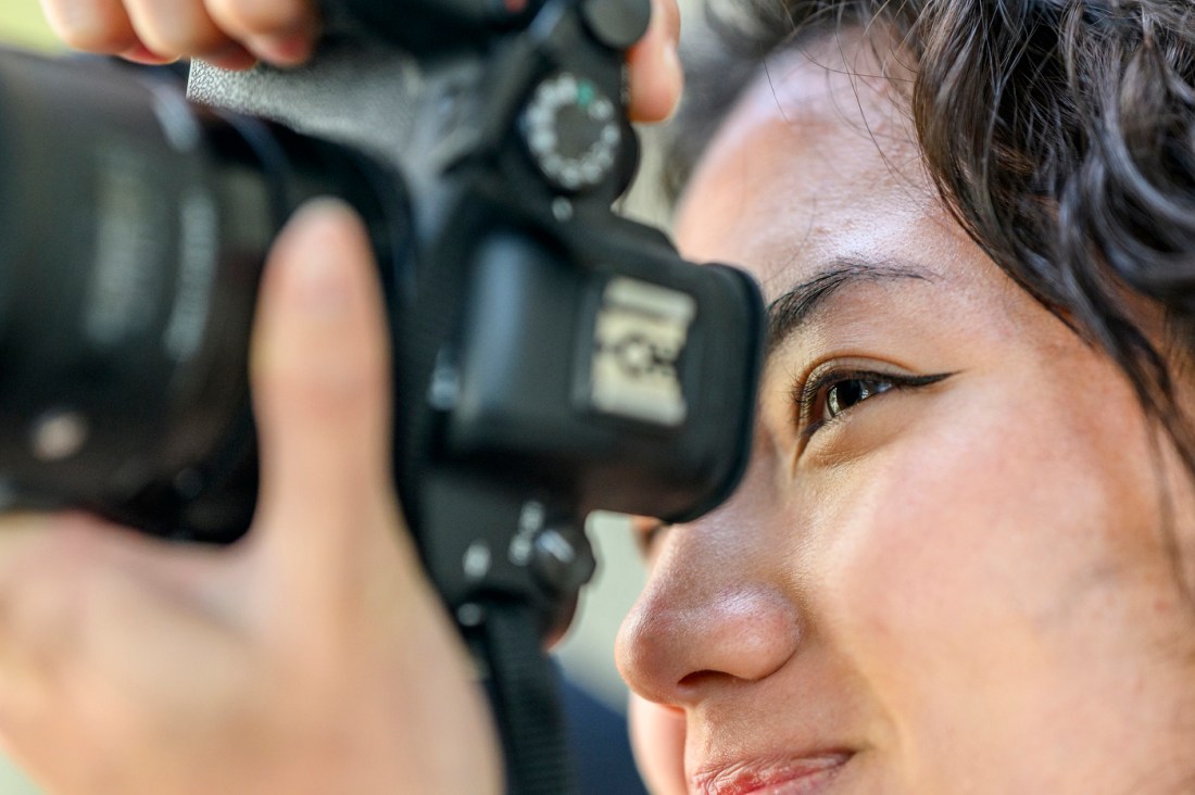 Close-up of Faith Nguyen looking through a camera viewfinder.