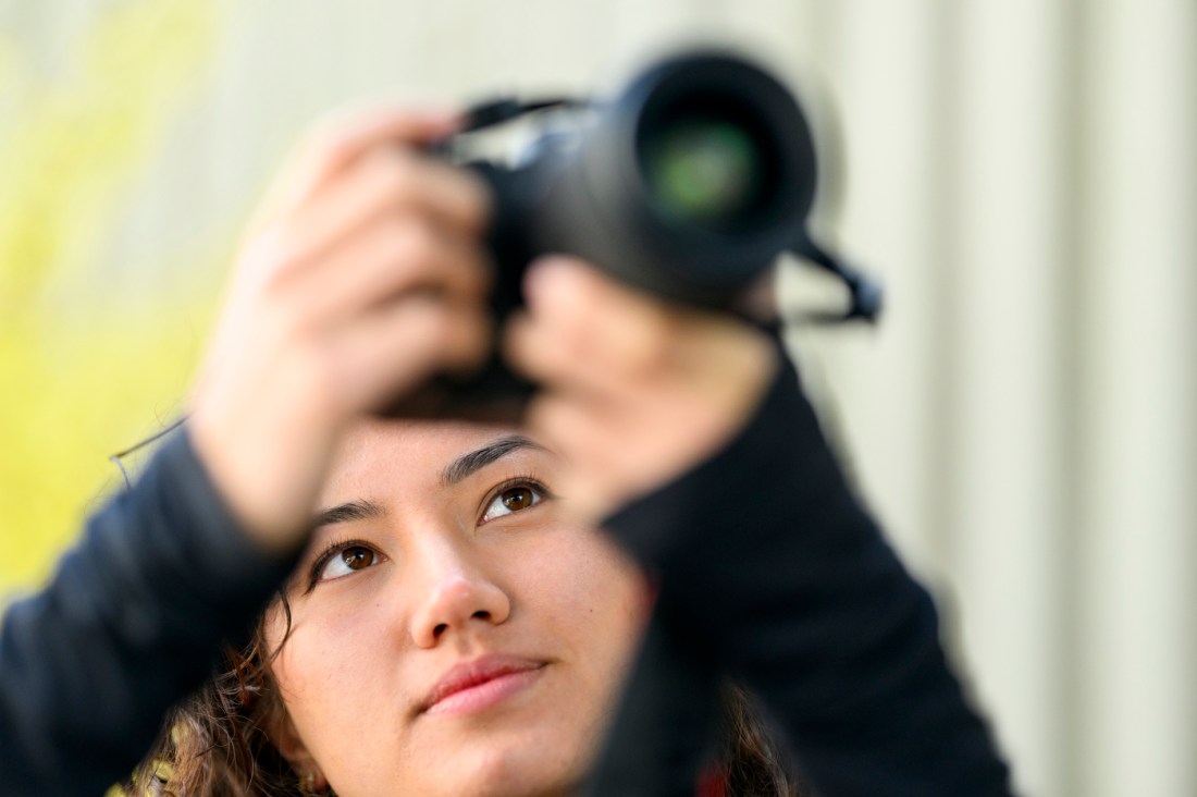 Faith Nguyen raises her camera to capture a photo outdoors.