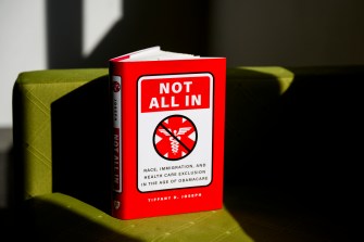 A book with a red cover that says 'Not All In' on it propped up on a green chair.