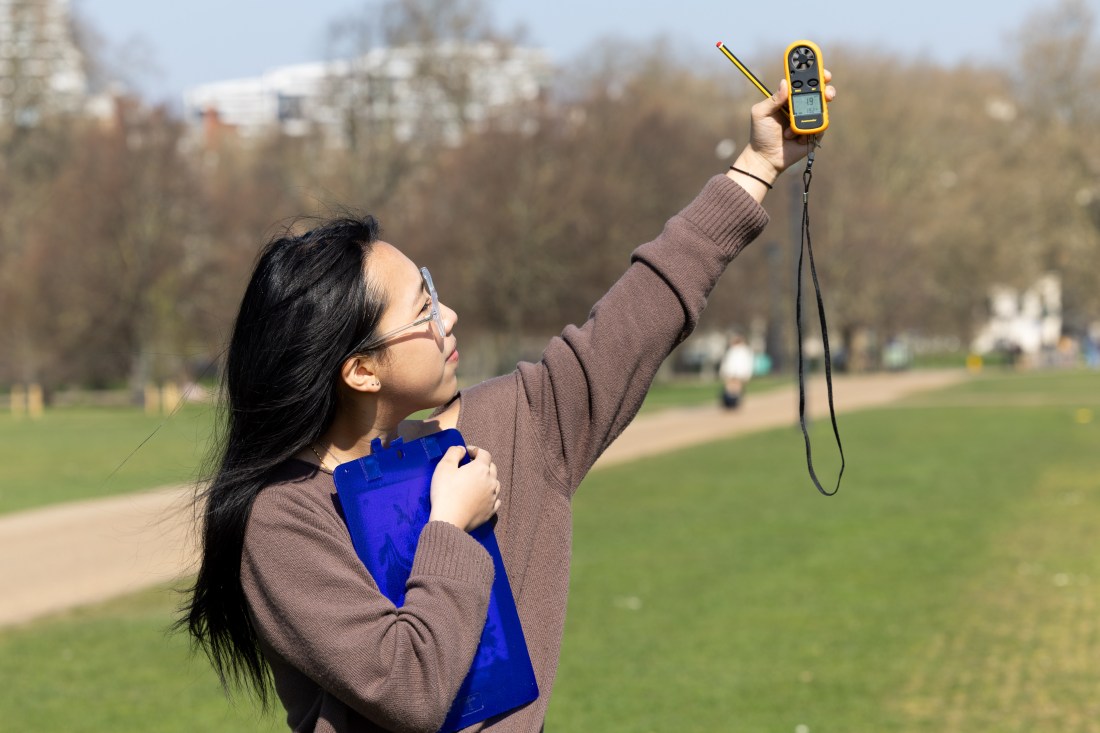 A student clutching a blue clipboard to their chest while holding up a yellow monitor in the air with their other hand.