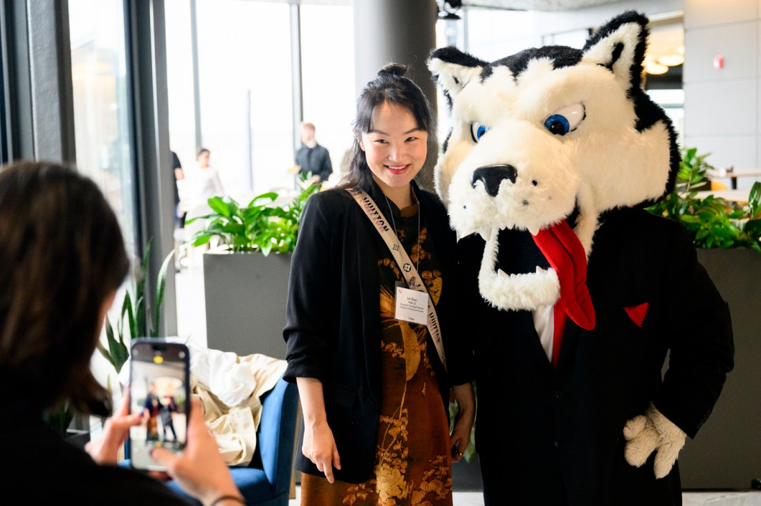 A member of the Northeastern community posing with Paws, the husky mascot.