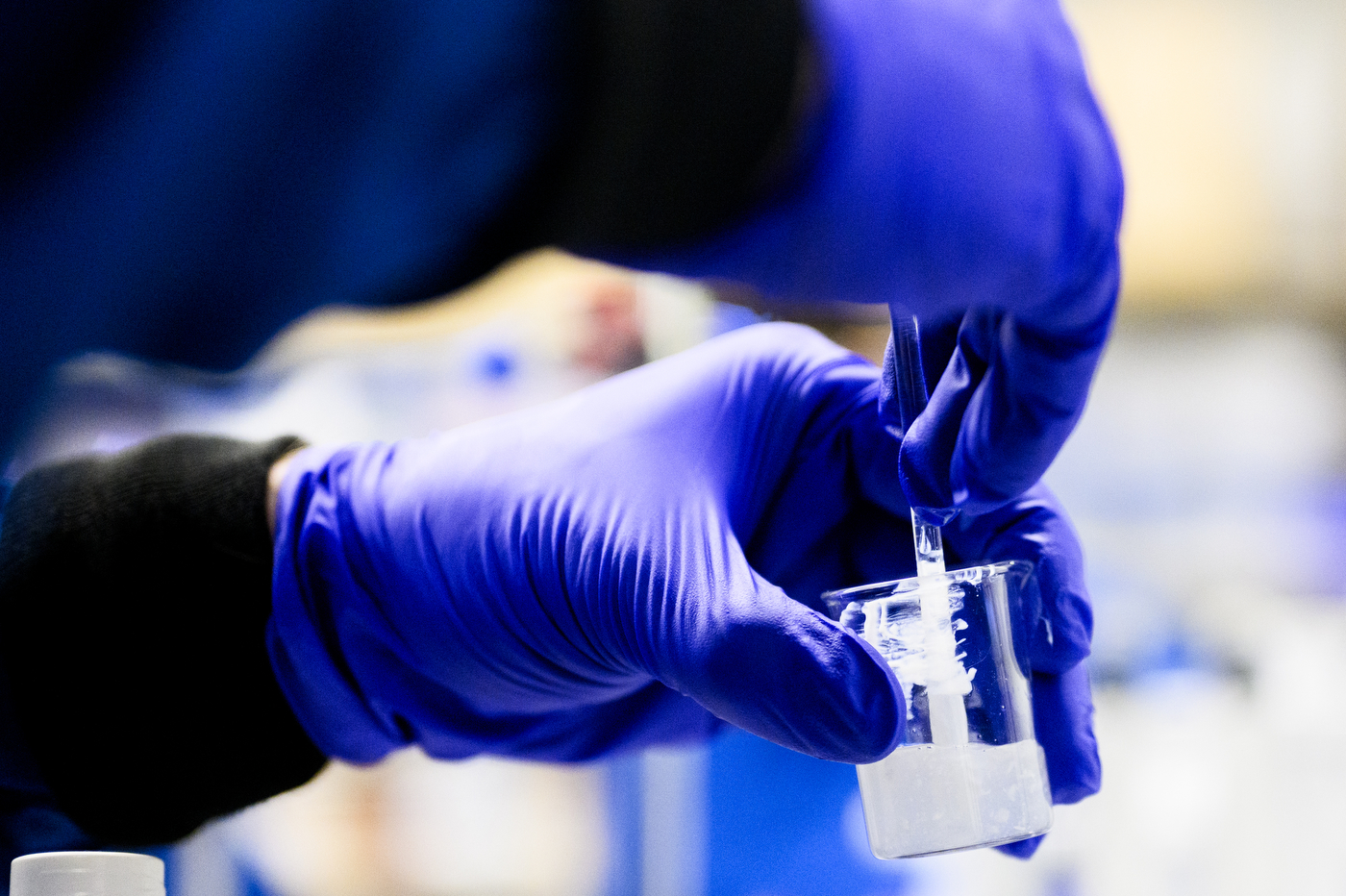 Blue gloved hands holding up a cosmetic product.