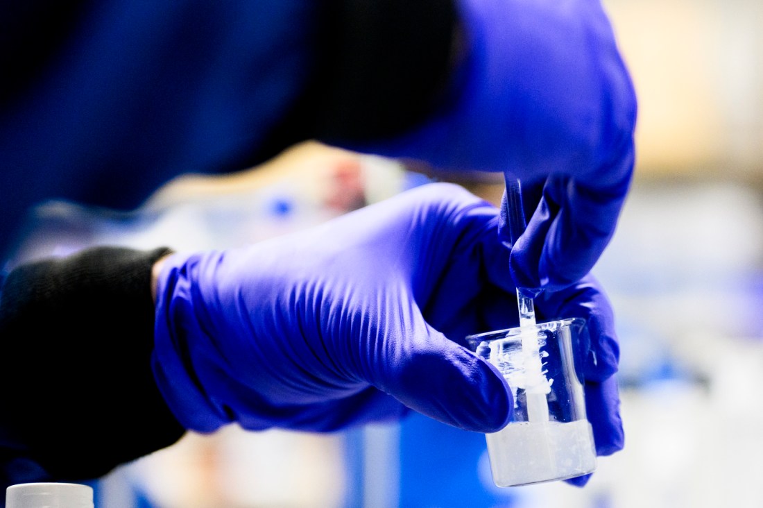 A gloved hand holding up a cosmetic product in the lab.