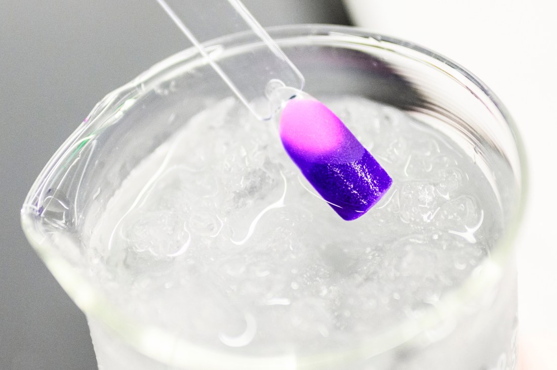 A pink and purple cosmetic sample being held over ice water in a beaker.