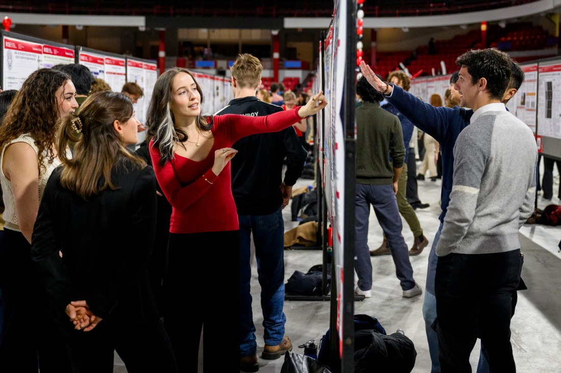 A student pointing to their poster while presenting at the RISE Expo.