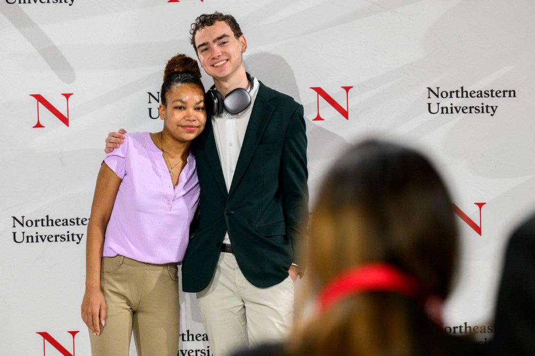 Two students posing for a photo in front of a Northeastern branded backdrop.