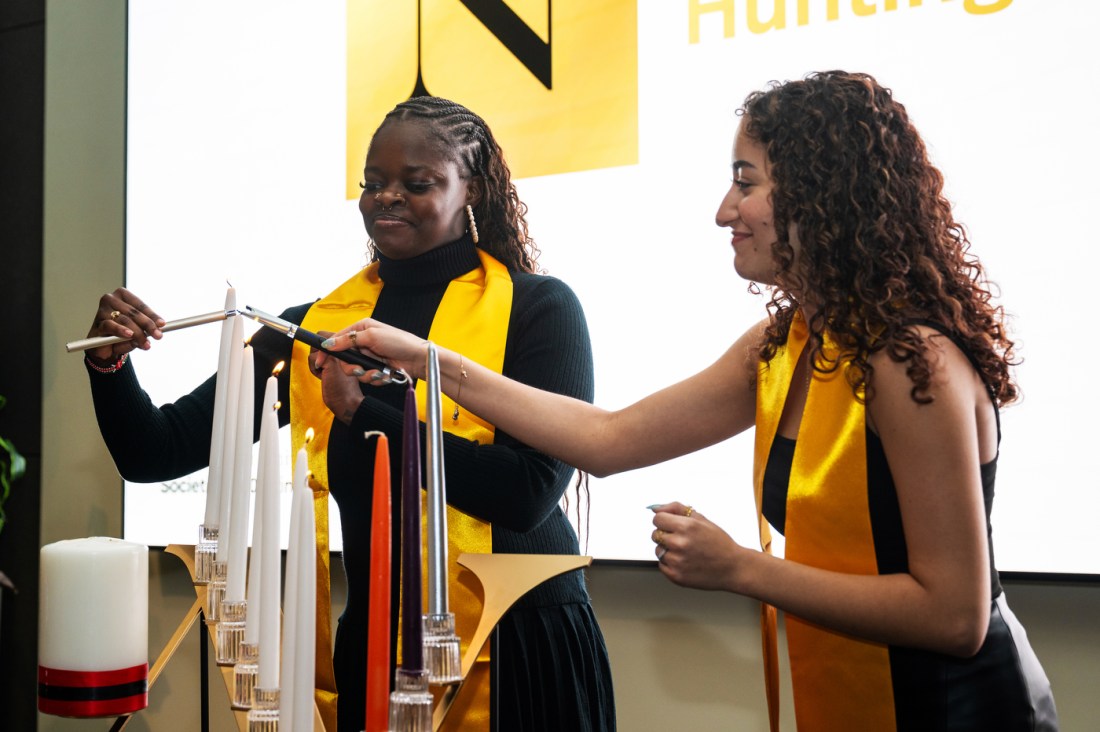 Two Huntington 100 Inductees wearing all black with yellow sashes around their necks light candles at the Huntington 100 Induction Ceremony.