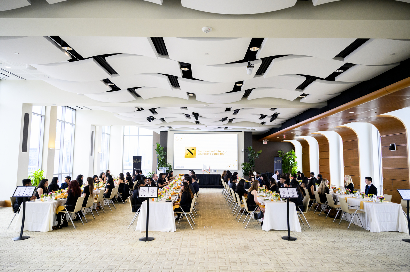 Four long tables placed next to each other with students wearing black sitting at them for the Laurel & Scroll Induction Ceremony.