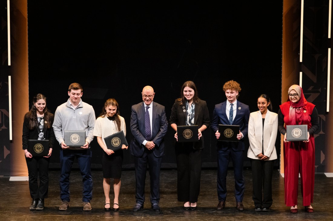 President Aoun standing on stage with a group of students holding honors.