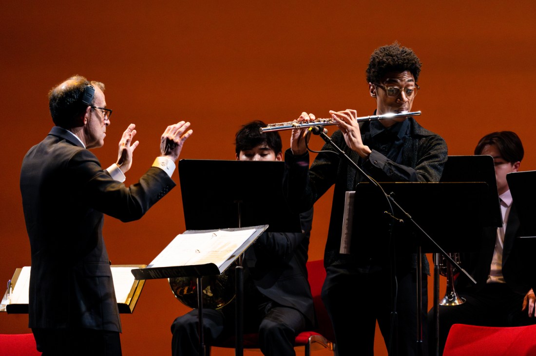 A conductor conducting a flute player who is standing and playing a solo.