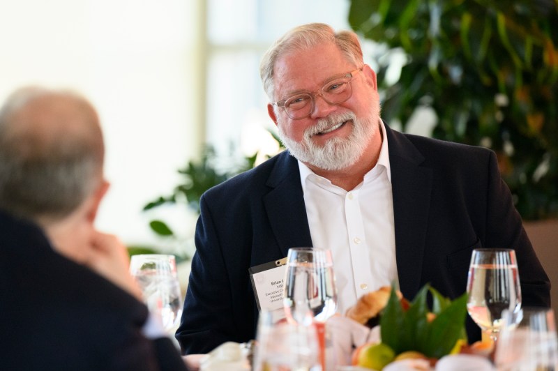A Northeastern community member sitting at a table smiling while talking with another community member.