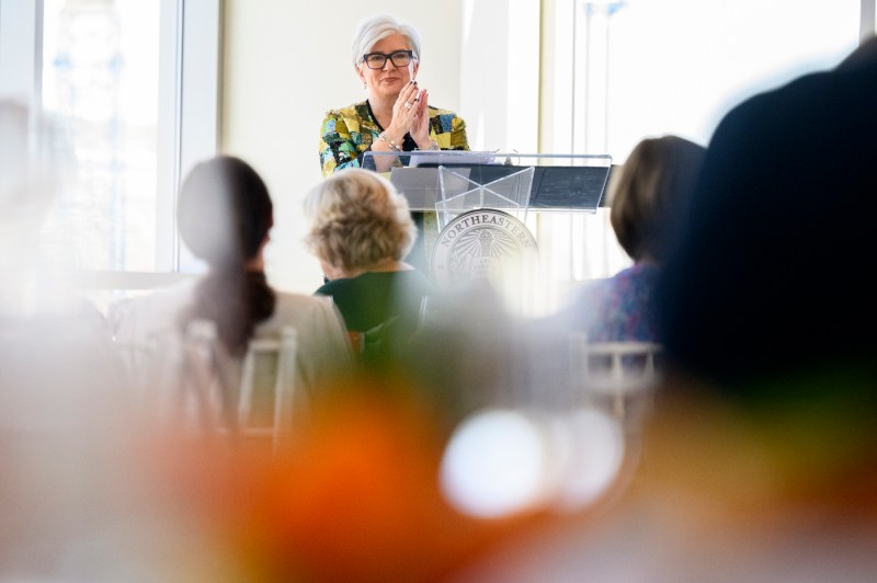A member of the Northeastern community standing at a clear podium at the 25 year associates brunch.